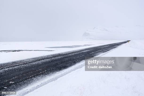 hringvegur ring road in iceland covered by ice and snow leading through winter landscape near höfn, southeast iceland, europe - reifenspur stock-fotos und bilder