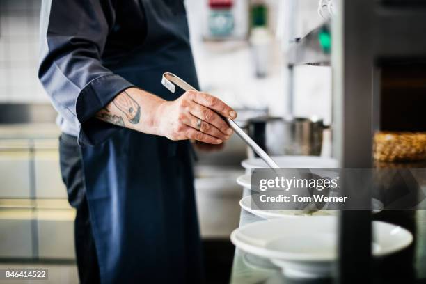 chef with tattoos ladling soup into bowls - cucharón fotografías e imágenes de stock