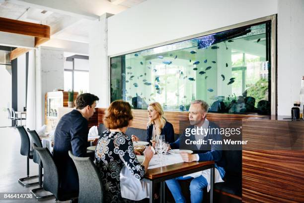 colleagues sitting beneath large fish tank in contemporary restaurant eating lunch - big tom stock-fotos und bilder