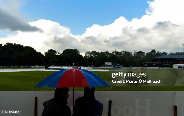 Belfast , Ireland - 13 September 2017; Spectators shelter from the rain under an umbrella as they await the result of a pitch inspectation before the...