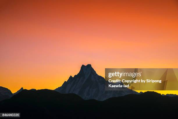 the peak of machapuchchre mountain with red-orange sky during sunrise from poon hill viewpoint. - hill range stock pictures, royalty-free photos & images