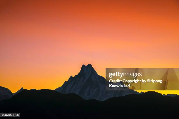 the peak of machapuchchre mountain with red-orange sky during sunrise from poon hill viewpoint. - nepal mountain stock pictures, royalty-free photos & images