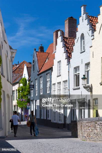 Couple walking past traditional architecture painted houses with crow-stepped gables by Peerdenstraat and Groenerei in Bruges, Belgium.