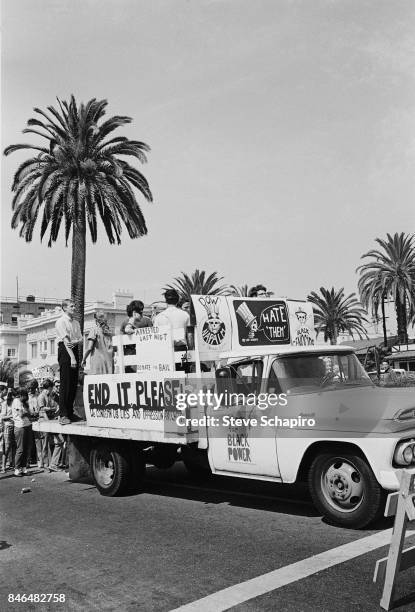 View of protestors, along with a flat-bed struck, during a anti-Vietnan war demonstration, Los Angeles, California, 1969. The truck features various...