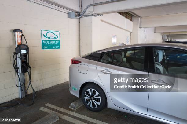 City-owned plug in hybrid Toyota Prius automobile is plugged in and charging at an electrical vehicle charging station in a municipal garage in...