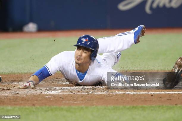 Darwin Barney of the Toronto Blue Jays slides across home plate to score the game-winning run on an RBI single by Richard Urena in the ninth inning...