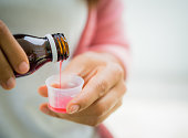 Closeup woman pouring medication or antipyretic syrup from bottle to cup.