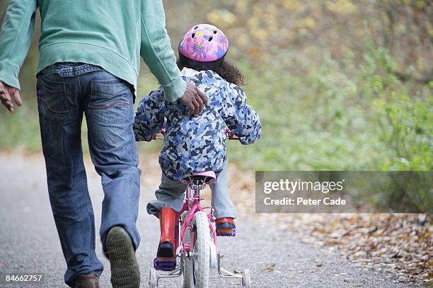 father pushing daughter on bike - bicycle daughter stock-fotos und bilder