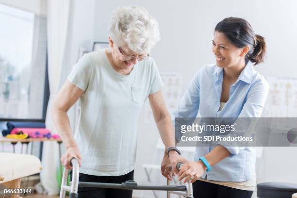 healthcare professional helps senior woman walk with a walker - rehab stock pictures, royalty-free photos & images