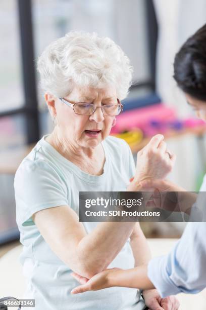 doctor examines senior woman's injured elbow - joint effort stock pictures, royalty-free photos & images