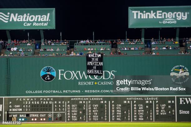 Fans display a sign that reads "Racism is as American as Baseball" over the Green Monster during the fourth inning of a game between the Boston Red...