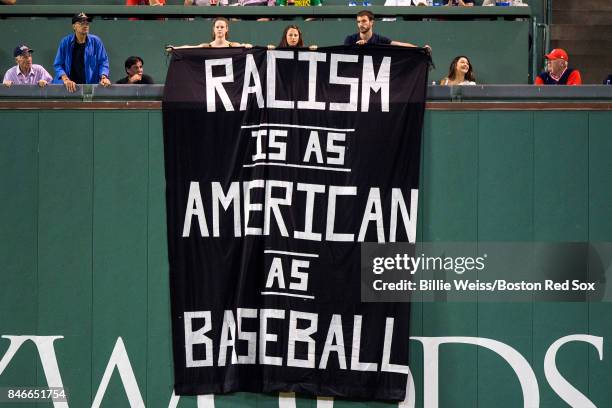 Fans display a sign that reads "Racism is as American as Baseball" over the Green Monster during the fourth inning of a game between the Boston Red...