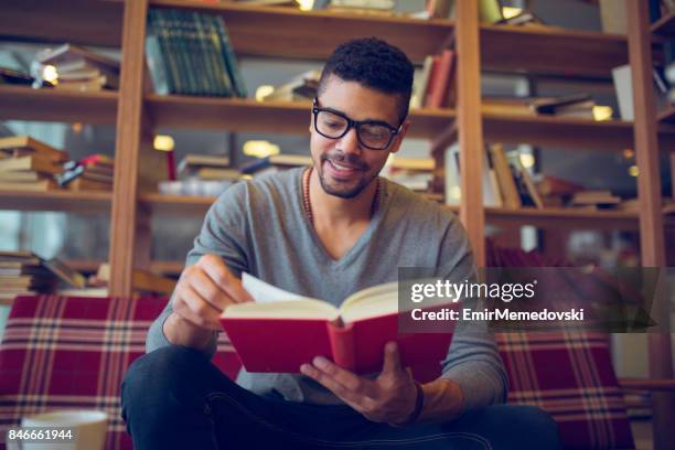 smiling african american student enjoying book reading in library - college student holding books stock pictures, royalty-free photos & images