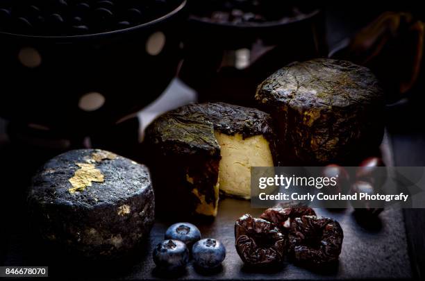 three goat cheeses chevre in various coating: (charcoal or ash, nettle leaves, grape leaves) with blueberries, prunes, olives and figs, served on the black slate board - ziegenkäse stock-fotos und bilder