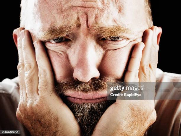 a middle-aged man grimaces, his head in his hands - midlife crisis stock pictures, royalty-free photos & images