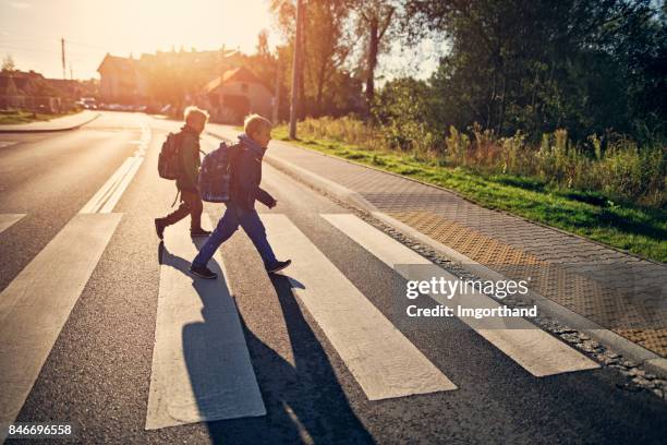 jongens van de school lopen op zebrapad op weg naar school - crossed stockfoto's en -beelden