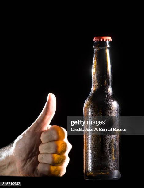 bottle of beer with the glass esmerilado with drops of water and the hand of a man with  thumb up on a black background - black thumbs up white background stock pictures, royalty-free photos & images