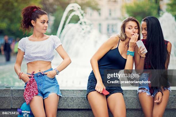 girlfriends are gossiping and bullying a girl at the front of a city fountain - cruel stock pictures, royalty-free photos & images