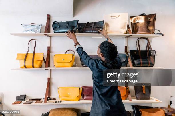 an entrepreneur handbag designer arranges her goods inside her store. - bolso fotografías e imágenes de stock