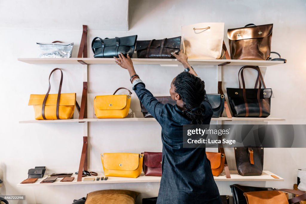 An entrepreneur handbag designer arranges her goods inside her store.