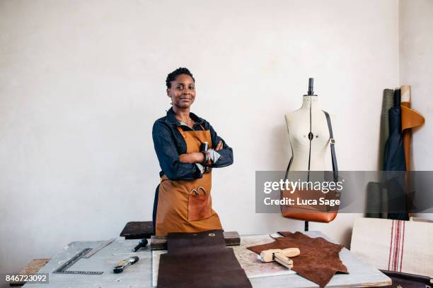 a leather craftswoman stands behind her desk, smiling to camera - smiling professional at work tools stock-fotos und bilder