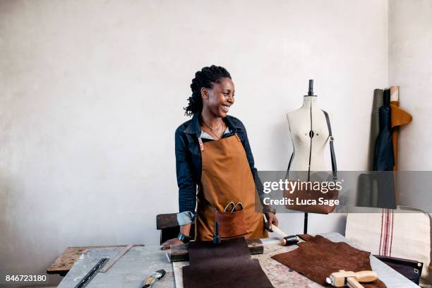 a leather craftswoman laughing behind her work bench - craftsman stock-fotos und bilder