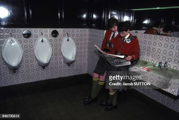 Jeunes gens en train de lire un journal dans les toilettes en avril 1983 en Irlande.