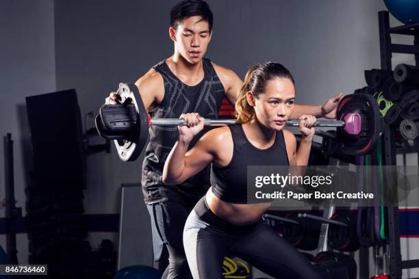 fit asian trainer assisting a good looking woman lifting a barbell - spotting bildbanksfoton och bilder