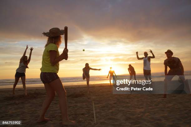 group of young people playing rounders on beach at sunset - baseball tee stock pictures, royalty-free photos & images