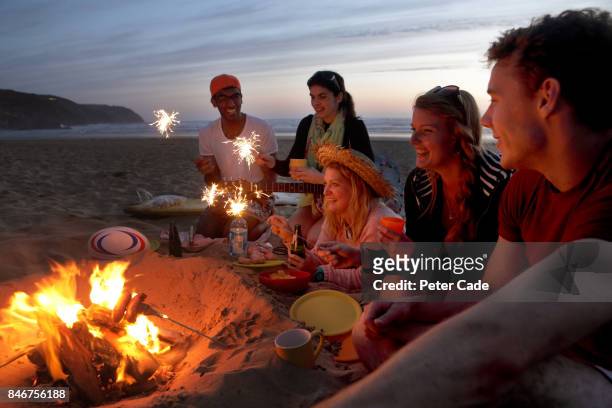 group of young people having fire on beach in the evening - beach holiday uk stock pictures, royalty-free photos & images