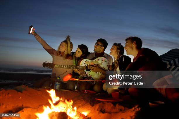 group of young people having fire on beach in the evening - feu plage photos et images de collection