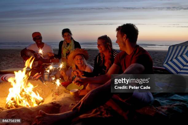 group of young people having fire on beach in the evening - camp fire stock pictures, royalty-free photos & images