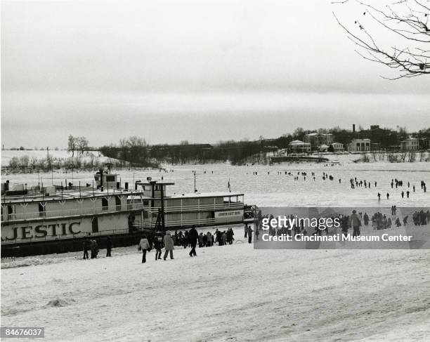 People walkalong on a frozen Ohio River as a Johnston party paddleboat and the boat Majestic lay docked on the bank, Cincinnati, Ohio, 1977.