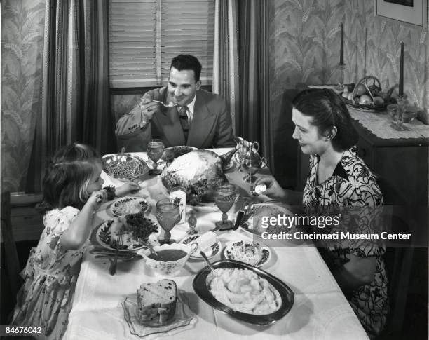Mother, father, and young girl sit down to their Thanksgiving dinner, ca.1945.