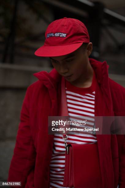 Guest is seen attending Marc Jacobs during New York Fashion Week wearing a red outfit with long coat, striped shirt, cross-body bag, and cap on...