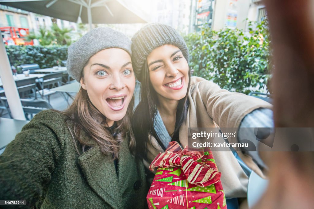 Gelukkig vriendinnen op sidewalk café een selfie nemen terwijl het doen van de kerstinkopen