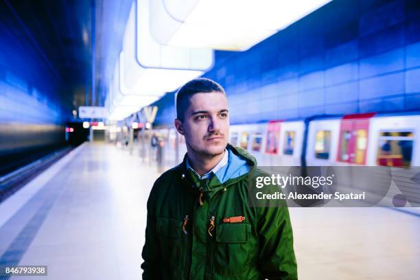 man in green jacket standing on a subway platfrom with blue lighting - german born stock pictures, royalty-free photos & images