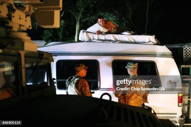 Soldiers from Delta Company, 1st Battallion, 124th Infantry, 53rd Infantry Brigade Combat Team talk to a man sleeping on top of a van in front of his...