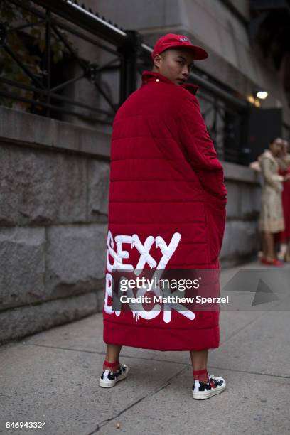 Guest is seen attending Marc Jacobs during New York Fashion Week wearing a red outfit with long coat, striped shirt, cross-body bag, and cap on...