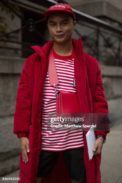 Guest is seen attending Marc Jacobs during New York Fashion Week wearing a red outfit with long coat, striped shirt, cross-body bag, and cap on...