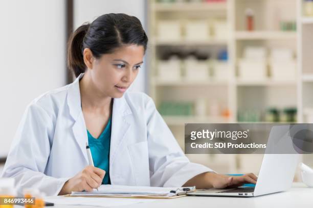 mid adult pharmacist uses laptop in pharmacy - medical writer stock pictures, royalty-free photos & images