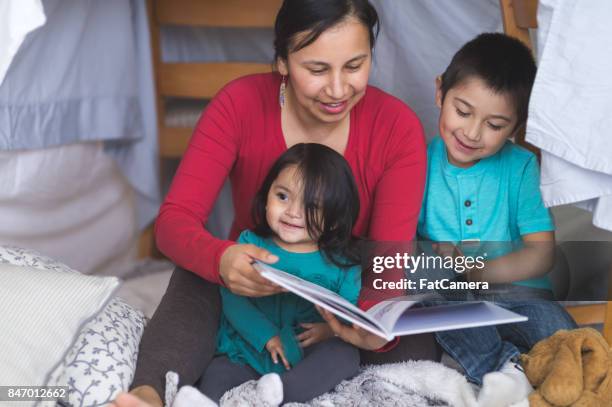 indianische mutter liest mit ihren beiden kindern unter provisorischen festung im wohnzimmer - gesellschaftsgeschichte stock-fotos und bilder