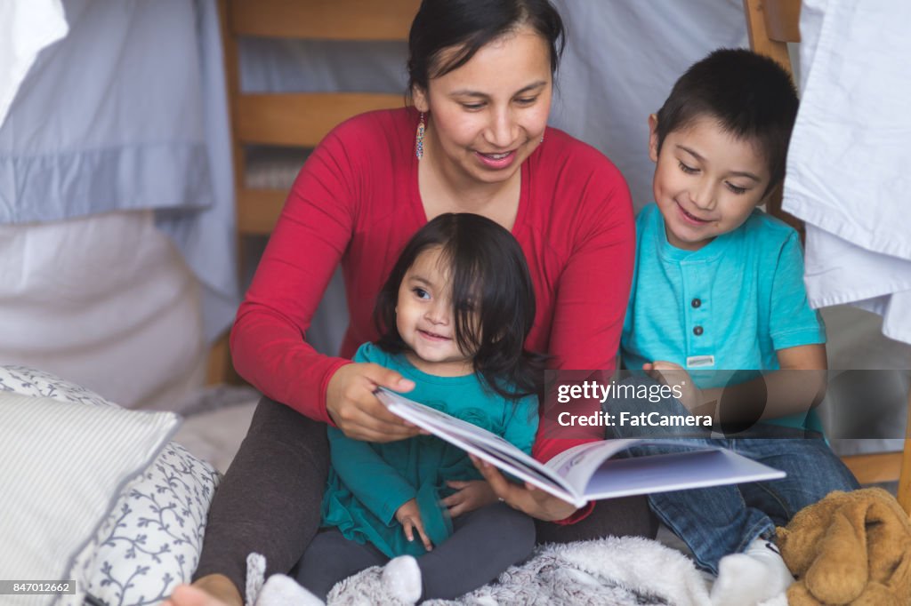 Native American mom reads with her two children under makeshift fort in living room