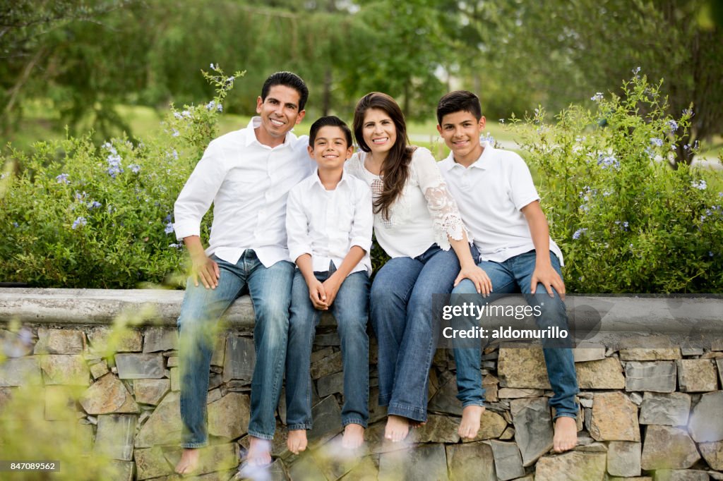 Latin family of four sitting on low wall and smiling