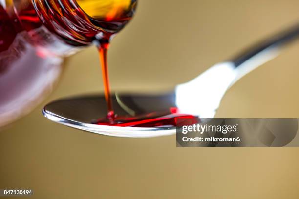 cough syrup being poured onto spoon. medical concept - jarabe fotografías e imágenes de stock