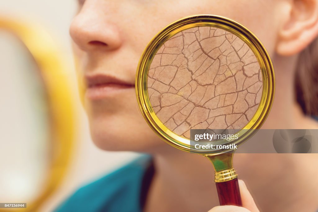 Aging and dry face skin concept - woman with magnifying glass