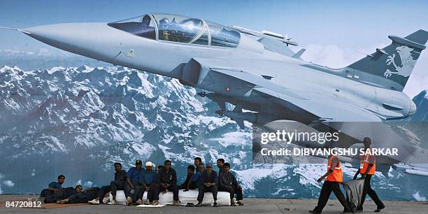 Indian labourers work and rest in front of a giant billboard of a Swedish Saab JAS39 Gripen multirole fighter aircraft at the Yelahanka Air Force...