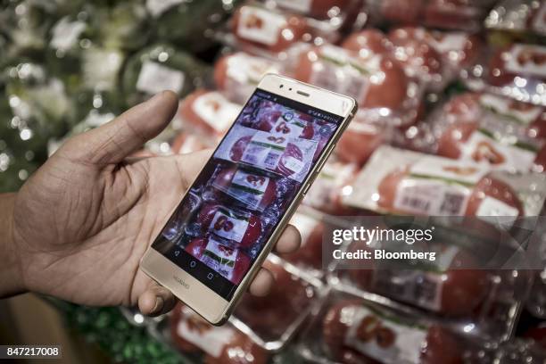 Customer displays the Hema application on a Huawei Technologies Co. Smartphone while shopping at an Alibaba Group Holding Ltd. Hema Store in...