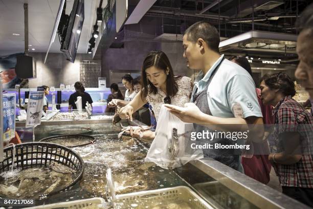 An employee assists a customer while she selects live seafood at an Alibaba Group Holding Ltd. Hema Store in Shanghai, China, on Tuesday, Sept. 12,...