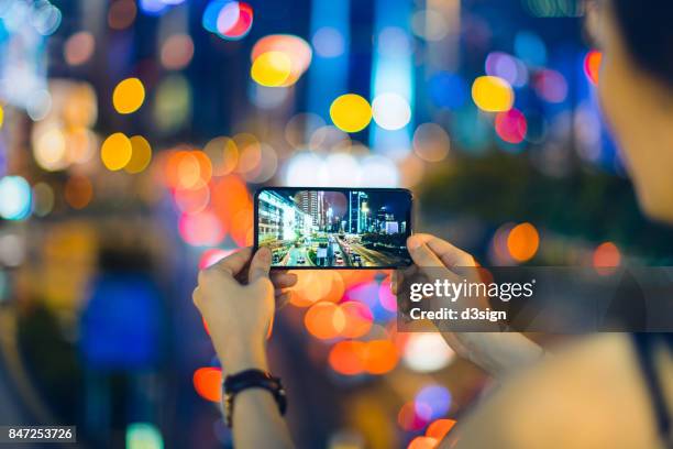 woman capturing city night scene with smartphone against illuminated street lights - woman capturing city night foto e immagini stock